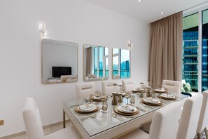 Une salle à manger moderne avec une table en verre, dressée pour six personnes, entourée de chaises blanches.