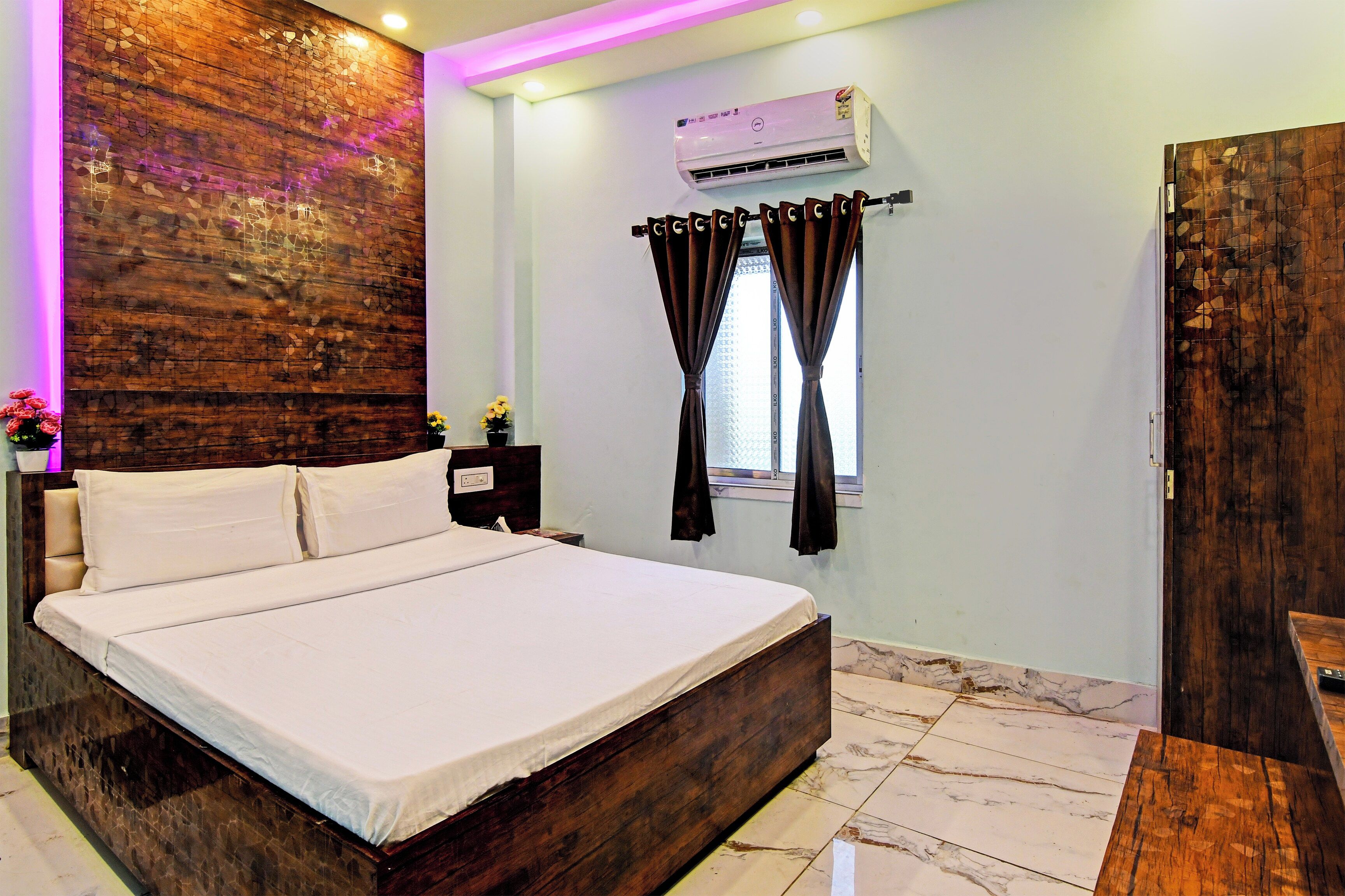 Une chambre avec un grand lit, un appareil de climatisation, une fenêtre avec des rideaux et un mur d’accent en bois.