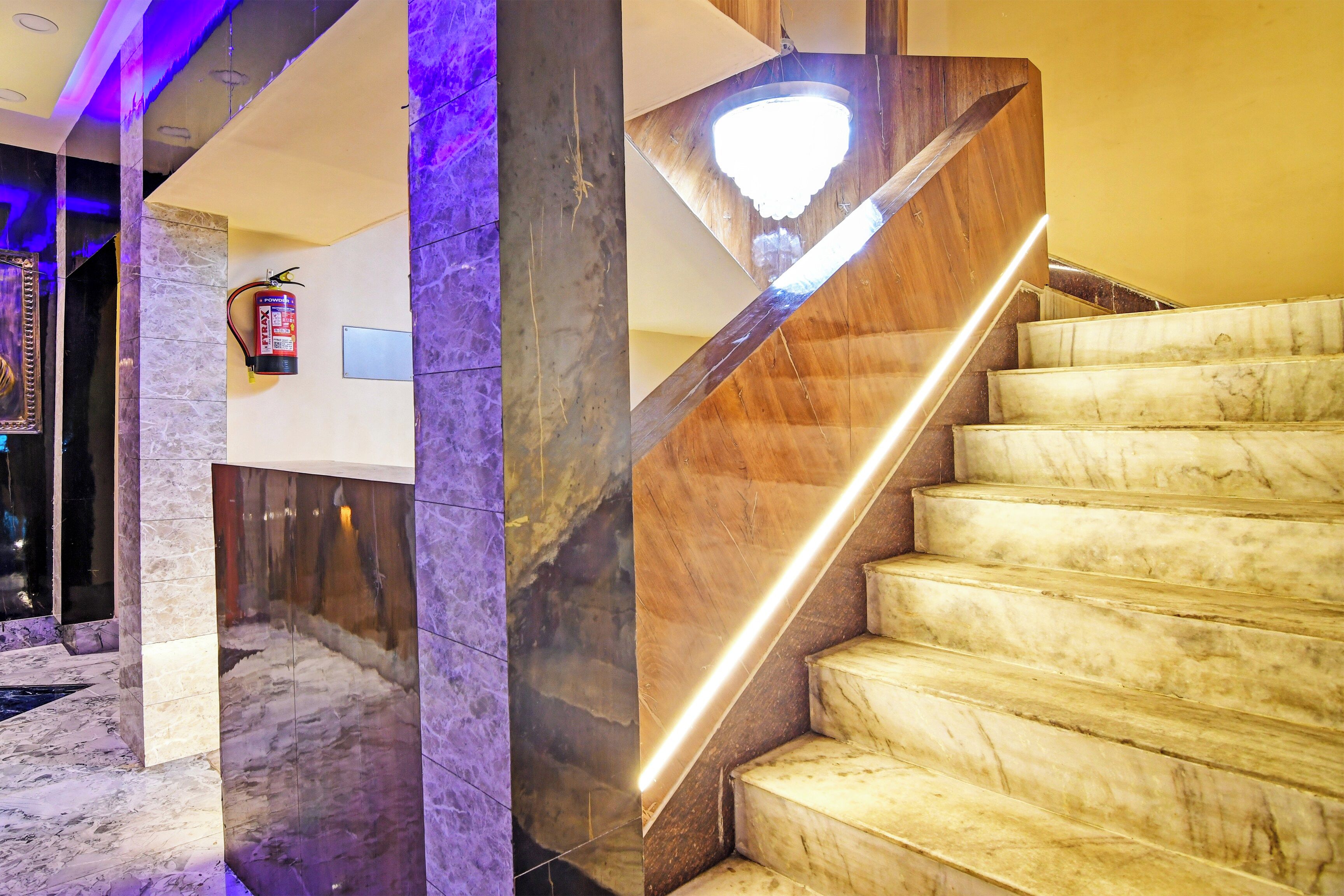 A marble staircase with a modern design, leading to a landing area with a fire extinguisher mounted on the wall.