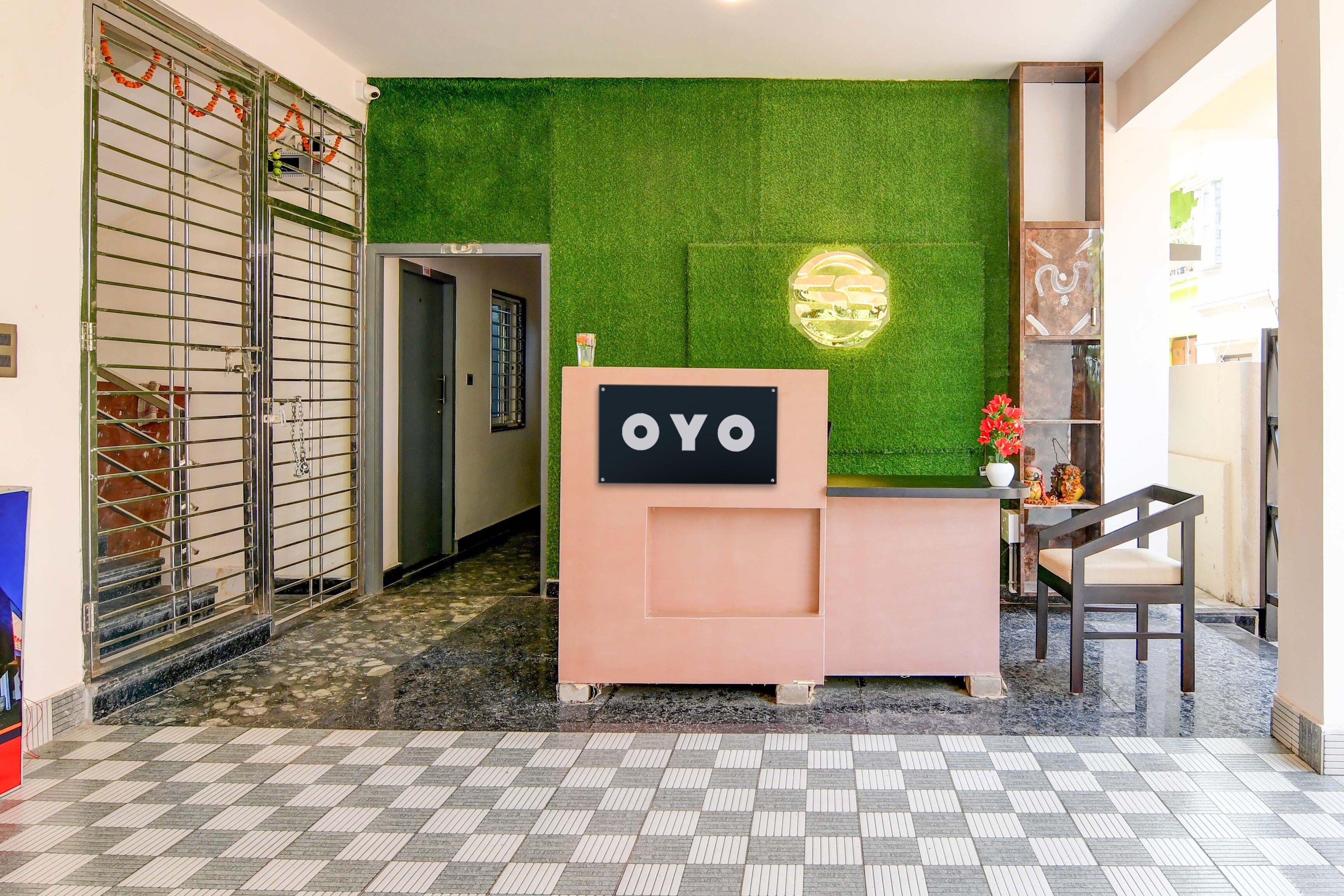 Zona de recepción con una pared verde, un mostrador de recepción con la etiqueta 'OYO' y una escalera que conduce a un piso superior.