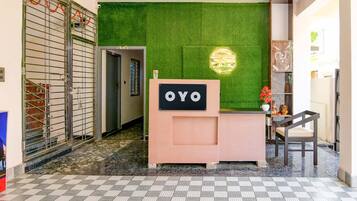 Zona de recepción con una pared verde, un mostrador de recepción con la etiqueta 'OYO' y una escalera que conduce a un piso superior.