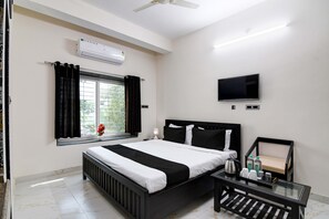 A hotel room with a bed, a TV, a window with curtains, and a radiator.