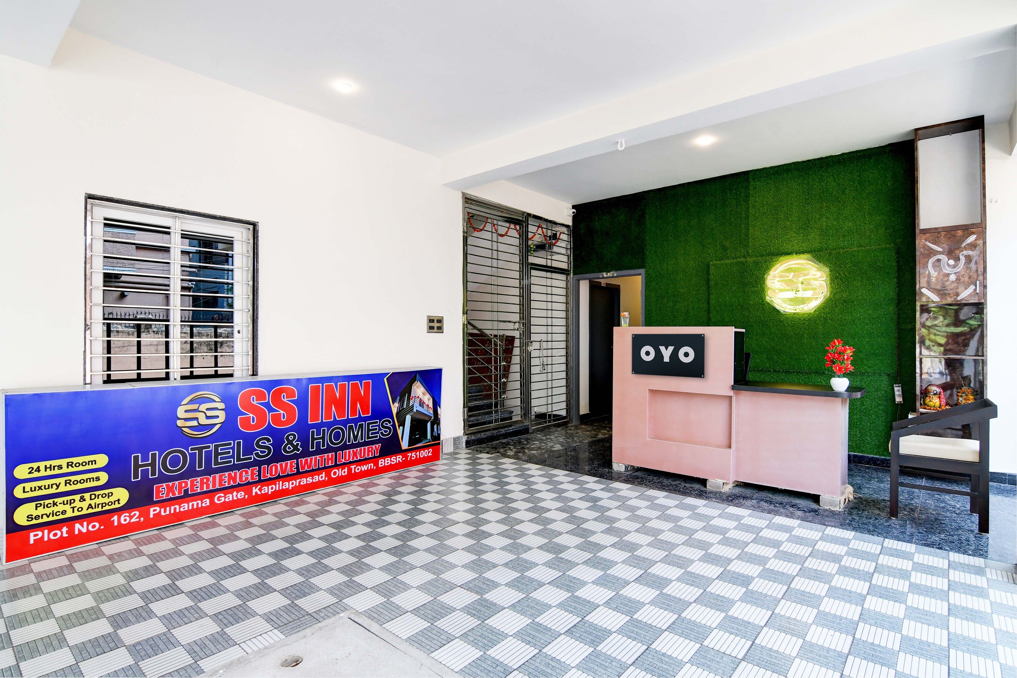 A hotel reception area with a check-in counter, a signboard advertising hotel services, and a green wall with a circular logo.