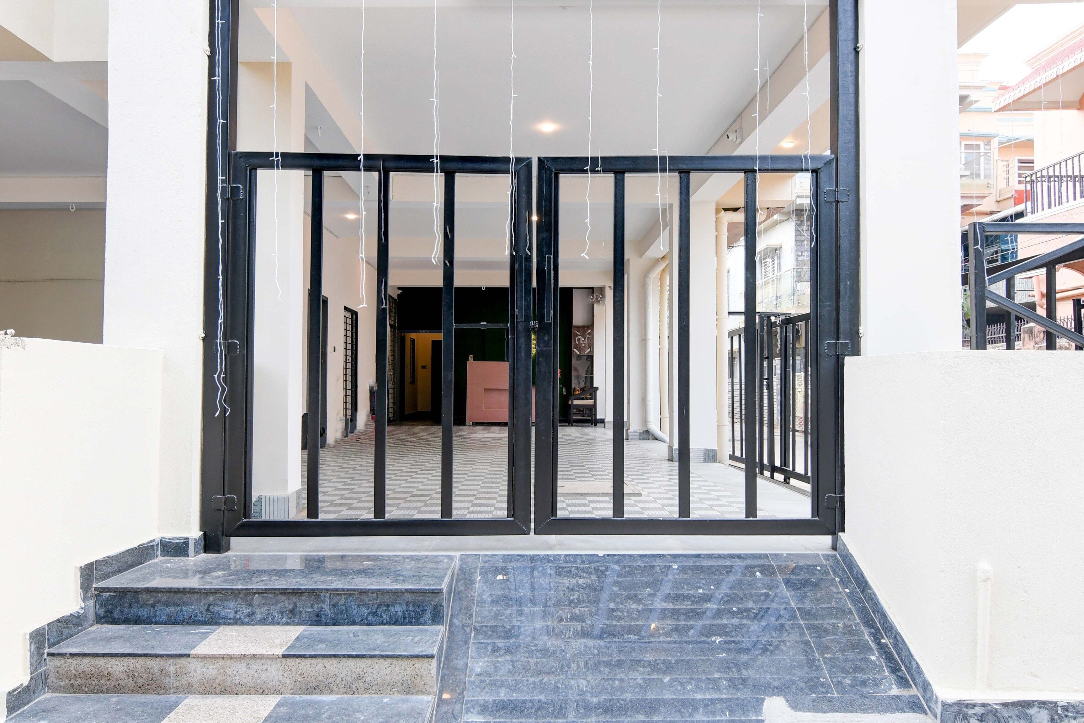 Entrada de hotel con una reja de metal negro, suelo de baldosas y una escalera que conduce a la entrada.