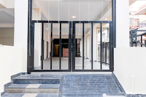 A hotel entrance with a black metal gate, a tiled floor, and a staircase leading up to the entrance.