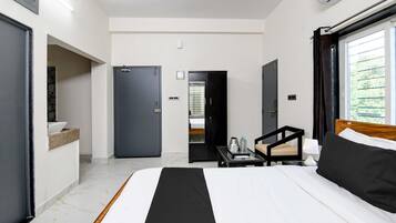 A hotel room with a bed, a small table with a lamp, a chair, and a view of greenery outside.