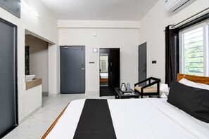 Habitació d'hotel amb un llit, una taula petita amb una làmpada, una cadira i vistes a espais verds.