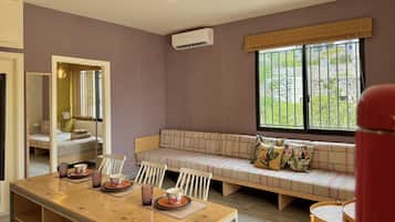Una habitación con una mesa de comedor de madera, un sofá con cojines, un espejo y una ventana con vista a la vegetación.