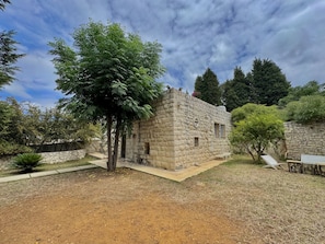 Edificio de piedra con un pequeño porche y un árbol frente a él.