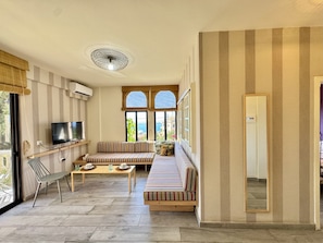 Uma sala de estar com sofá, televisão e janela com vista.