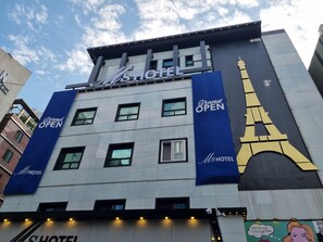 Un edificio de hotel con un cartel llamativo que dice 'MS HOTEL' y un gran banderín azul que anuncia 'Gran APERTURA'.