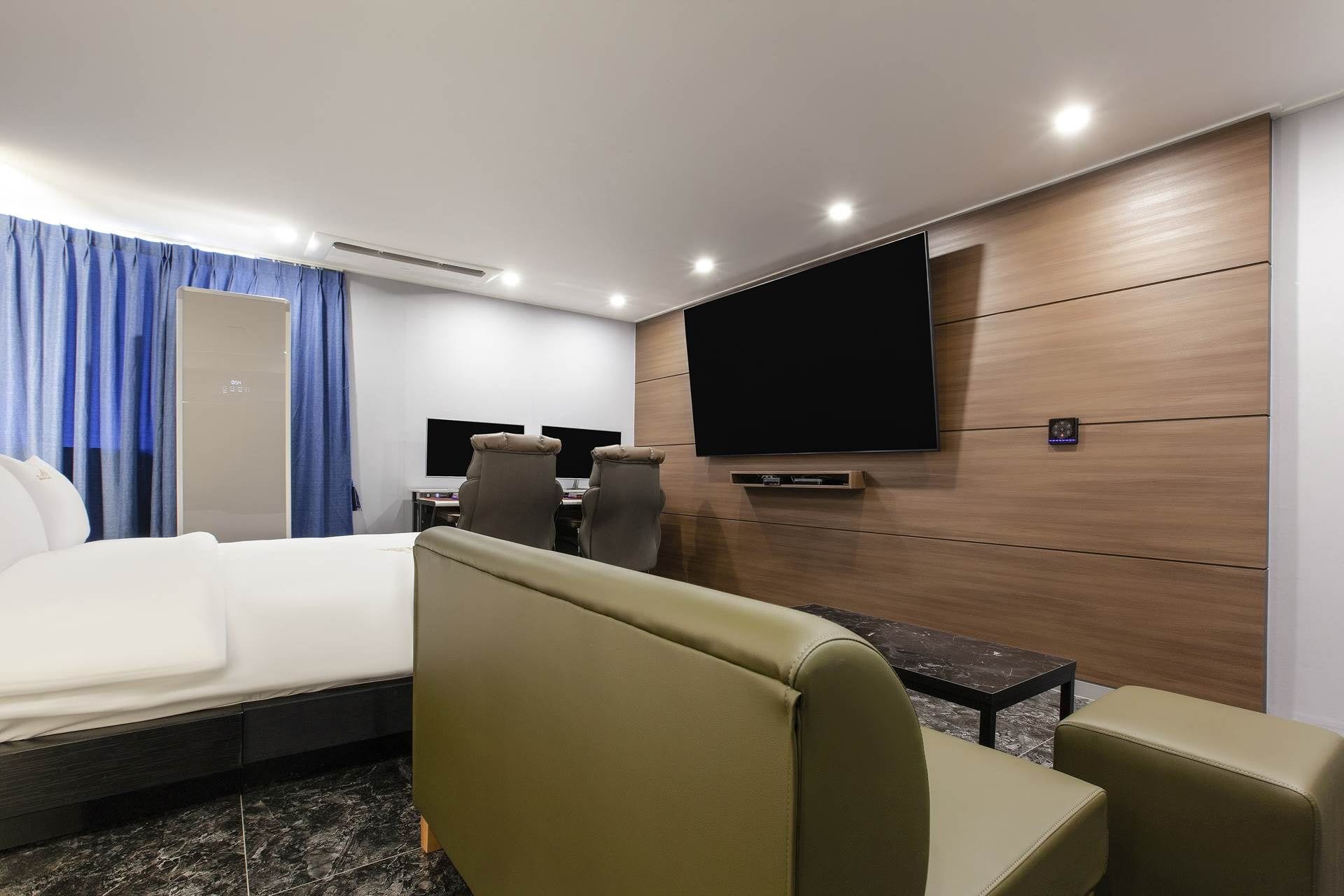 Habitación de hotel con cama, dos sillones, un escritorio con computadora, televisor de pantalla plana en la pared y una mesita.