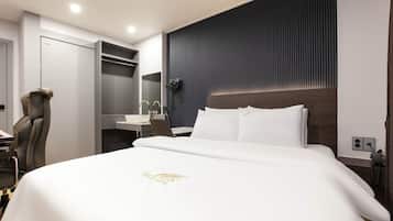 A hotel room with a bed, a desk, a chair, a mirror, and a bathroom vanity.