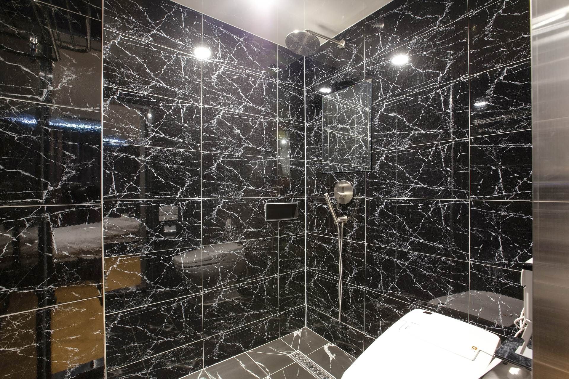 A bathroom with black marble walls, a white toilet, and a shower area.