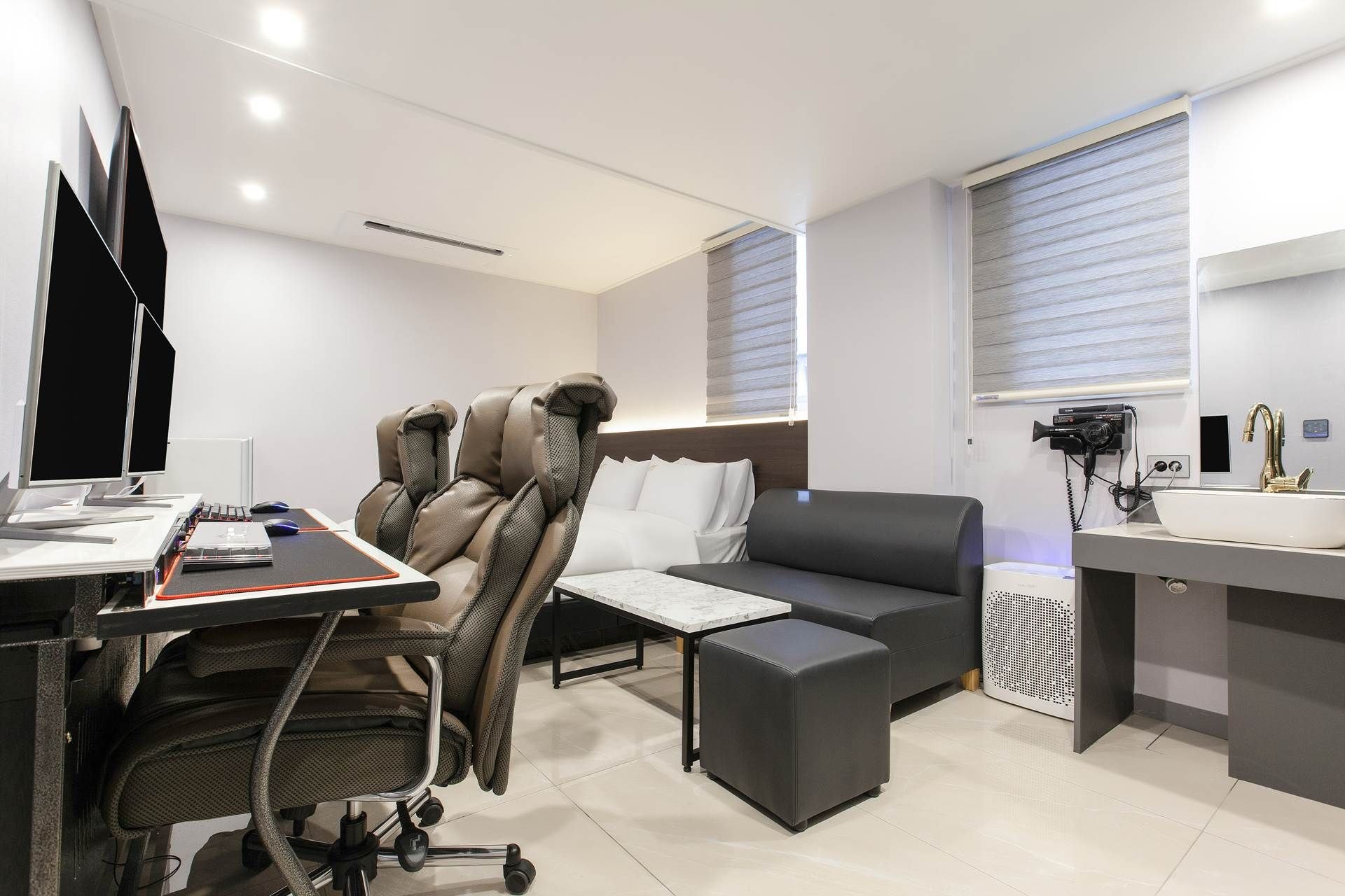 A modern office space with a desk, computer, ergonomic chairs, a sofa, and a kitchenette area.