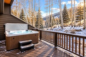 A wooden deck with a hot tub and a wooden bench, overlooking a snowy landscape with trees and mountains. - NEW Queen Esther Deluxe 4 BR Deer Valley Townhome with Hot Tub | QET-2366 by KBM (Park City)