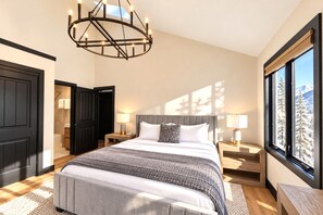 Ein modernes Schlafzimmer mit einem großen Bett, Nachttischlampen, einer Pendelleuchte und Blick auf einen verschneiten Berg.