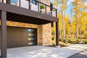 A modern two-story house with a stone facade, a dark garage door, and a balcony with a view of a forest in autumn. - NEW Queen Esther Deluxe 4 BR Deer Valley Townhome with Hot Tub | QET-2366 by KBM (Park City)