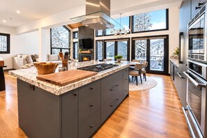 A modern kitchen with a large island, built-in appliances, and a view of a snowy landscape through large windows. - NEW Queen Esther Deluxe 4 BR Deer Valley Townhome with Hot Tub | QET-2366 by KBM (Park City)
