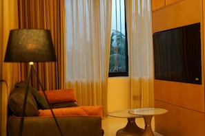 A room with a sofa, a lamp, a table, and a TV.