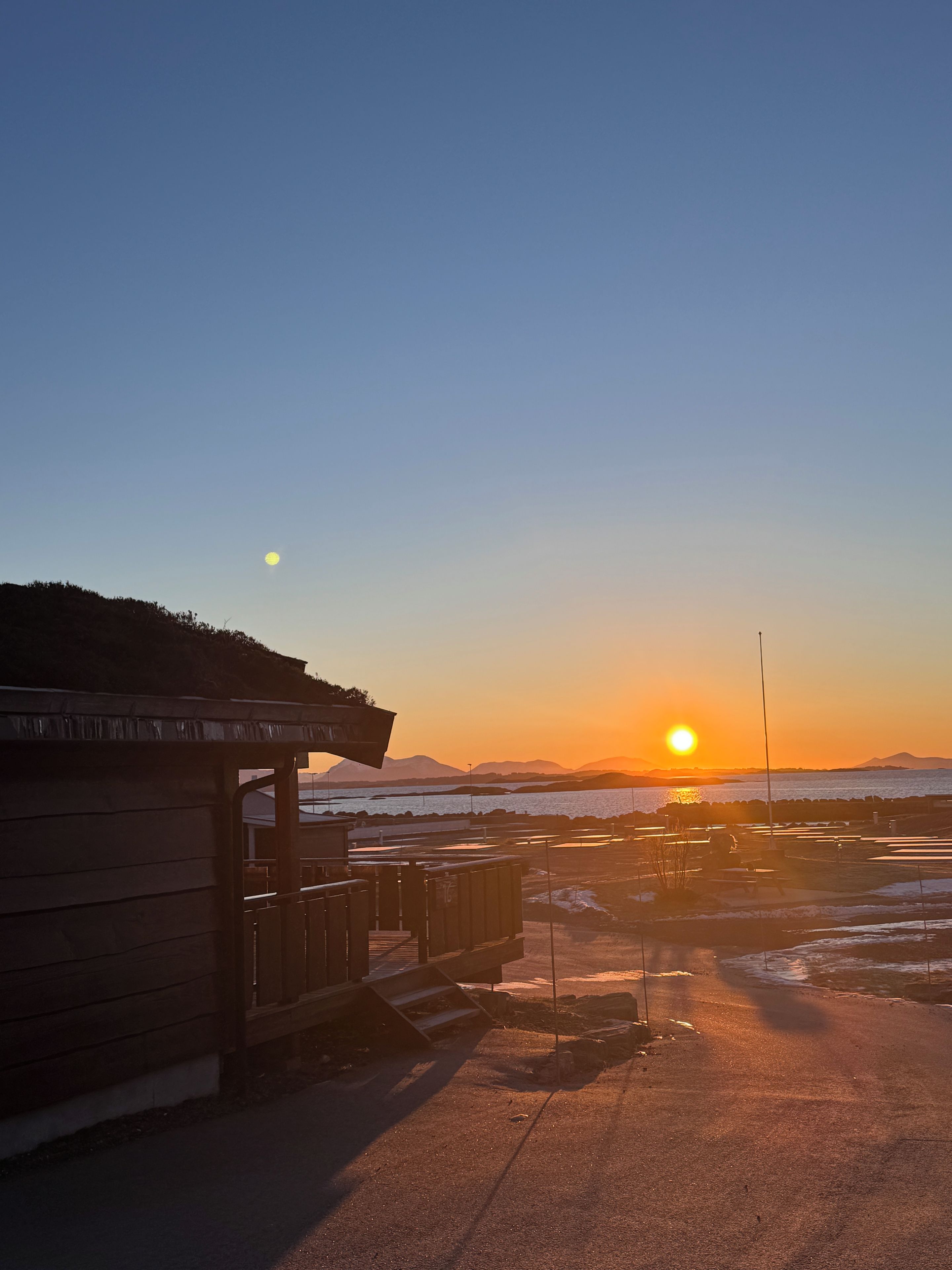 Un bâtiment en bois doté d’un porche couvert, d’une zone pavée et offrant une vue sur le coucher de soleil sur l’eau.
