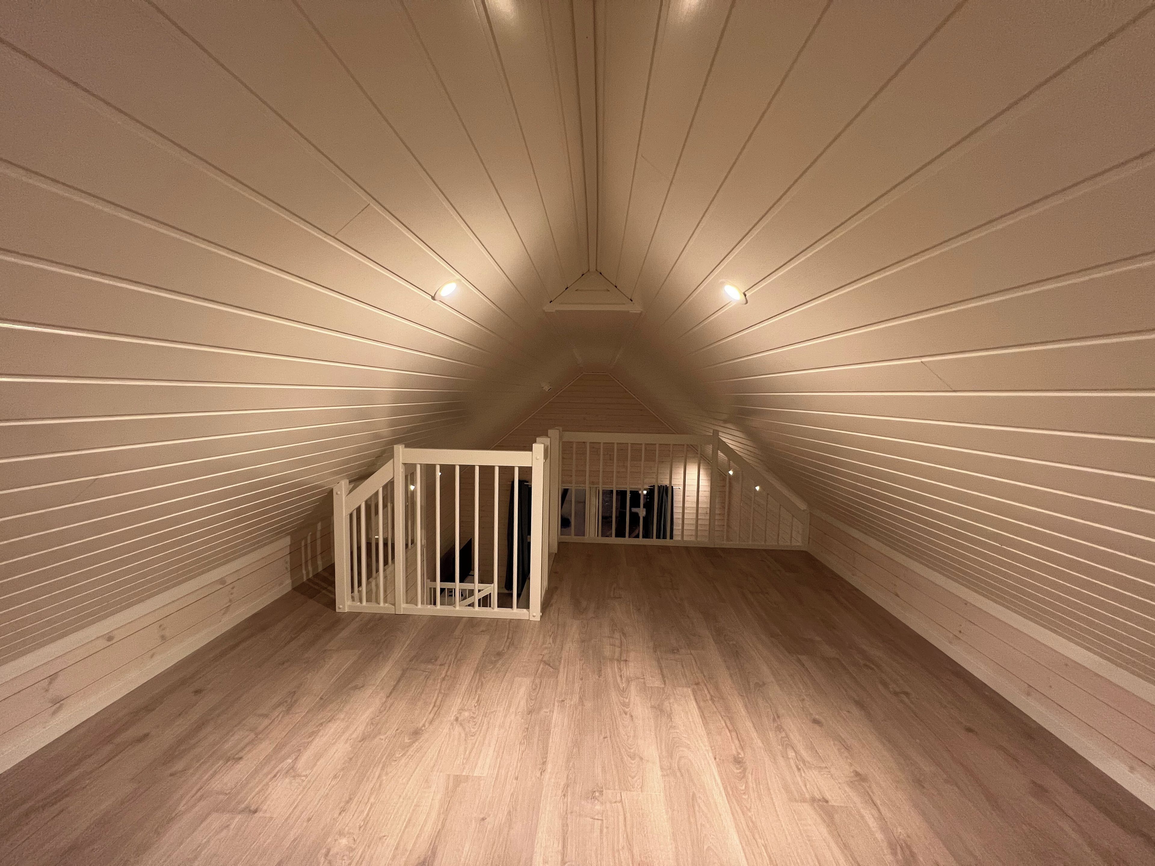 Une pièce mansardée avec des lambris en bois aux murs et au plafond, un plancher en bois et un petit escalier menant à une porte.