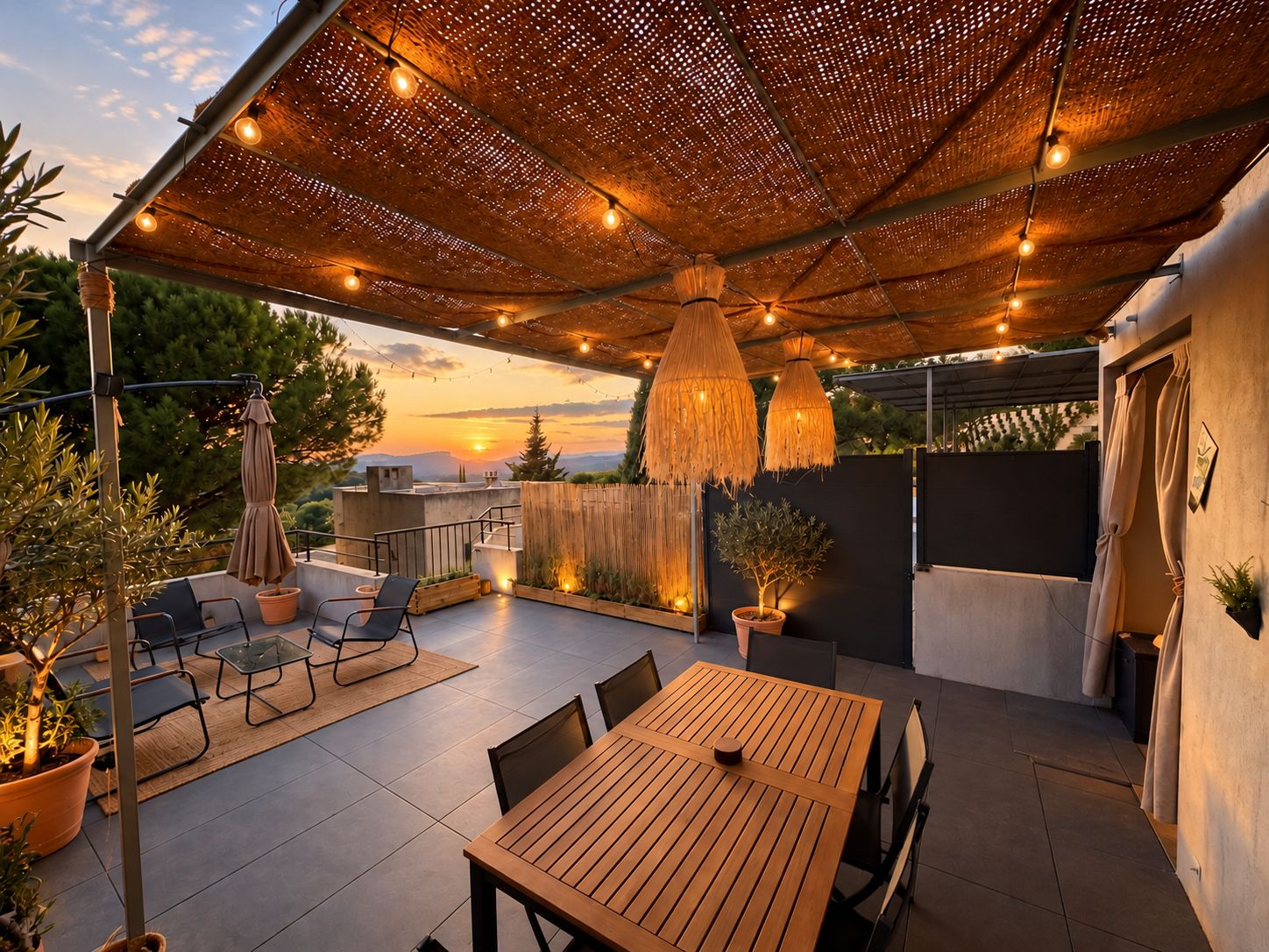 Une terrasse extérieure avec une table et des chaises en bois, un luminaire suspendu et une vue sur le coucher de soleil.