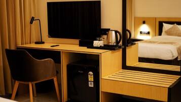 Habitación de hotel con escritorio, silla, televisor, cafetera y cama con cabecera.
