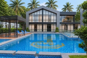 Ein modernes Gebäude mit Schwimmbad, Liegestühlen und Palmen.