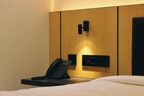 A hotel room with a bed, a bedside telephone, and a control panel on the wall.