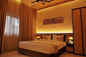 Ein Hotelzimmer mit einem großen Bett, einem Kopfteil mit Beleuchtung, einem Nachttisch mit Telefon und einem an der Wand hängenden Kunstwerk.