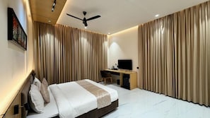 Una habitación de hotel con cama, escritorio, televisor y cortinas.