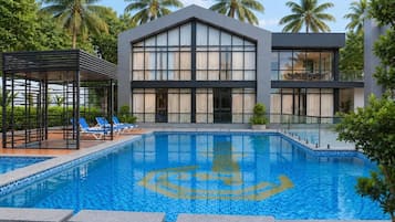 Ein modernes Gebäude mit Schwimmbad, Liegestühlen und Palmen.