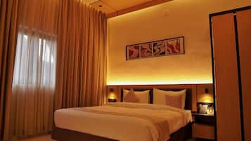 A hotel room with a large bed, a headboard with a light, a bedside table with a phone, and a wall-mounted artwork.