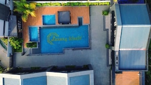 An aerial view of a hotel with a swimming pool, a wooden deck, and a sign that reads 'Luxury World.'