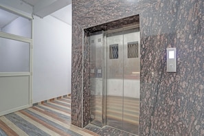 Un ascensor con detalles metálicos, una pared con textura similar al mármol y un suelo a rayas.