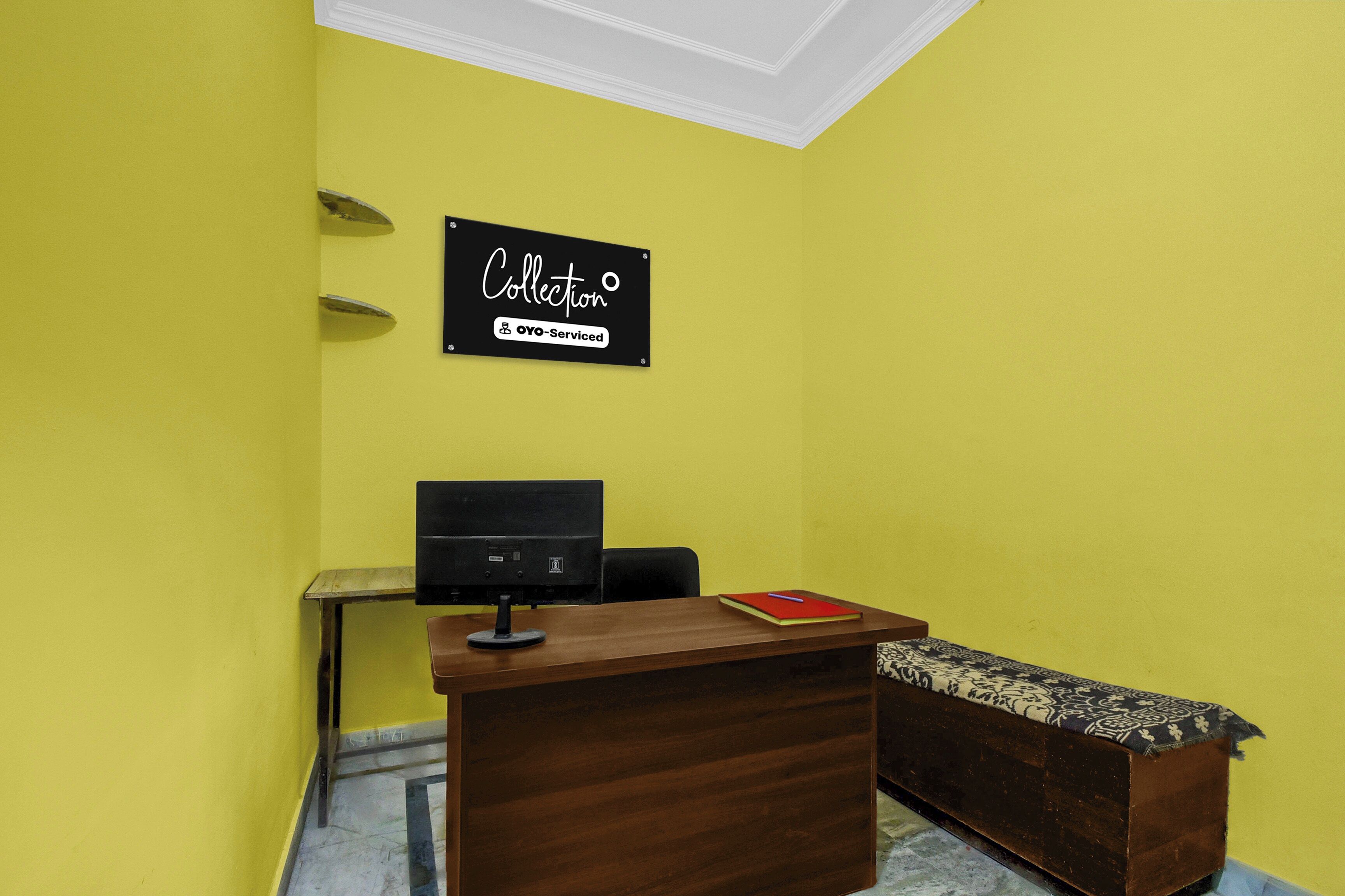 A reception desk with a sign above it, a computer monitor, a small table, a chair, and a bench.