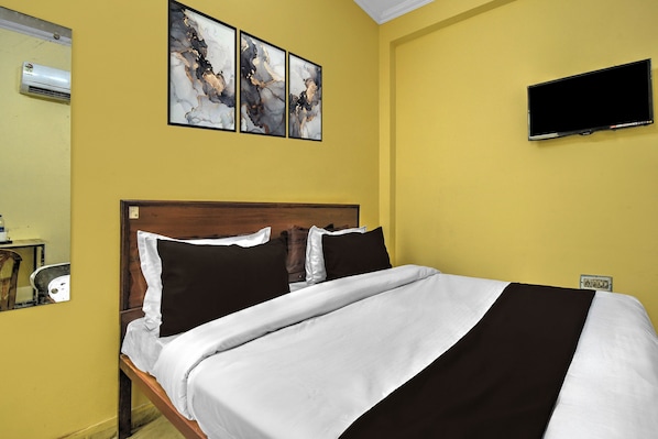 Quarto de hotel com uma cama, uma televisão de tela plana e três quadros abstratos na parede.