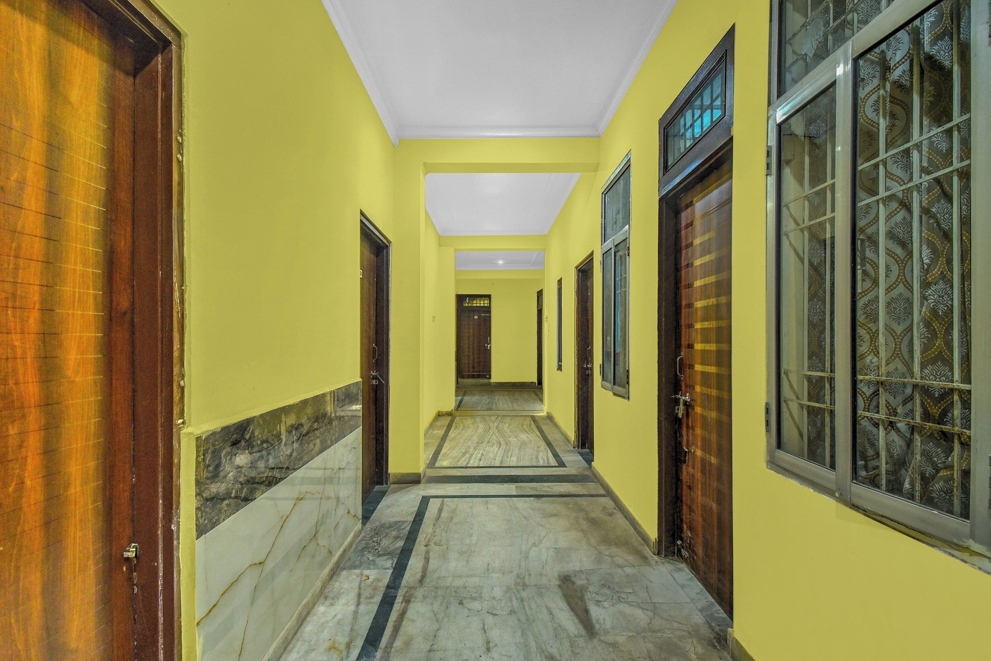 A hallway with yellow walls, wooden doors, and patterned windows.