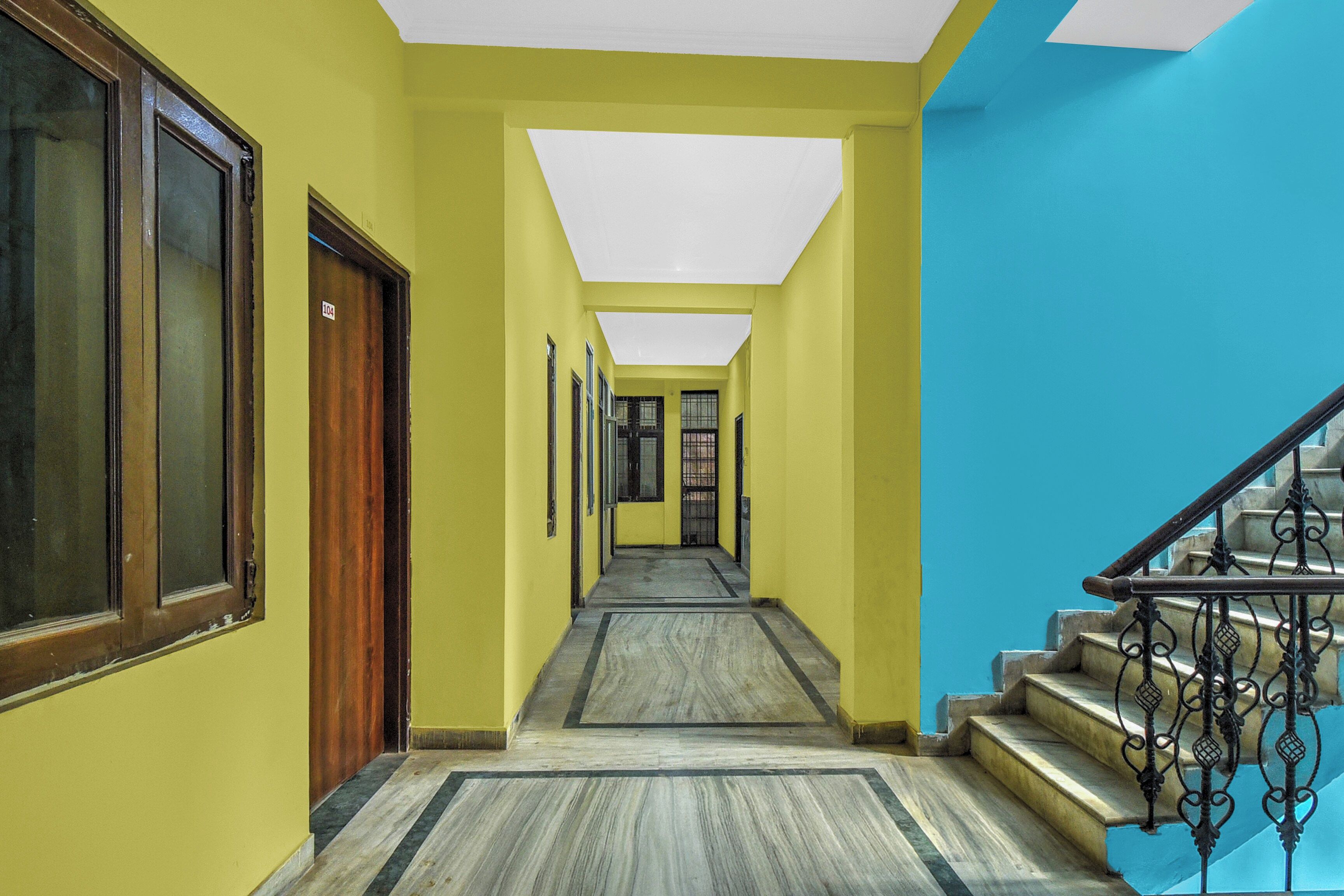 A hallway with a wooden door, a staircase with metal railings, and a tiled floor.