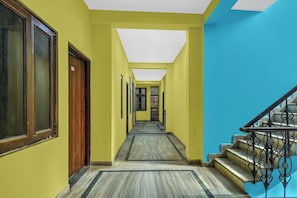 Um corredor com porta de madeira, escada com corrimão de metal e piso revestido de azulejos.
