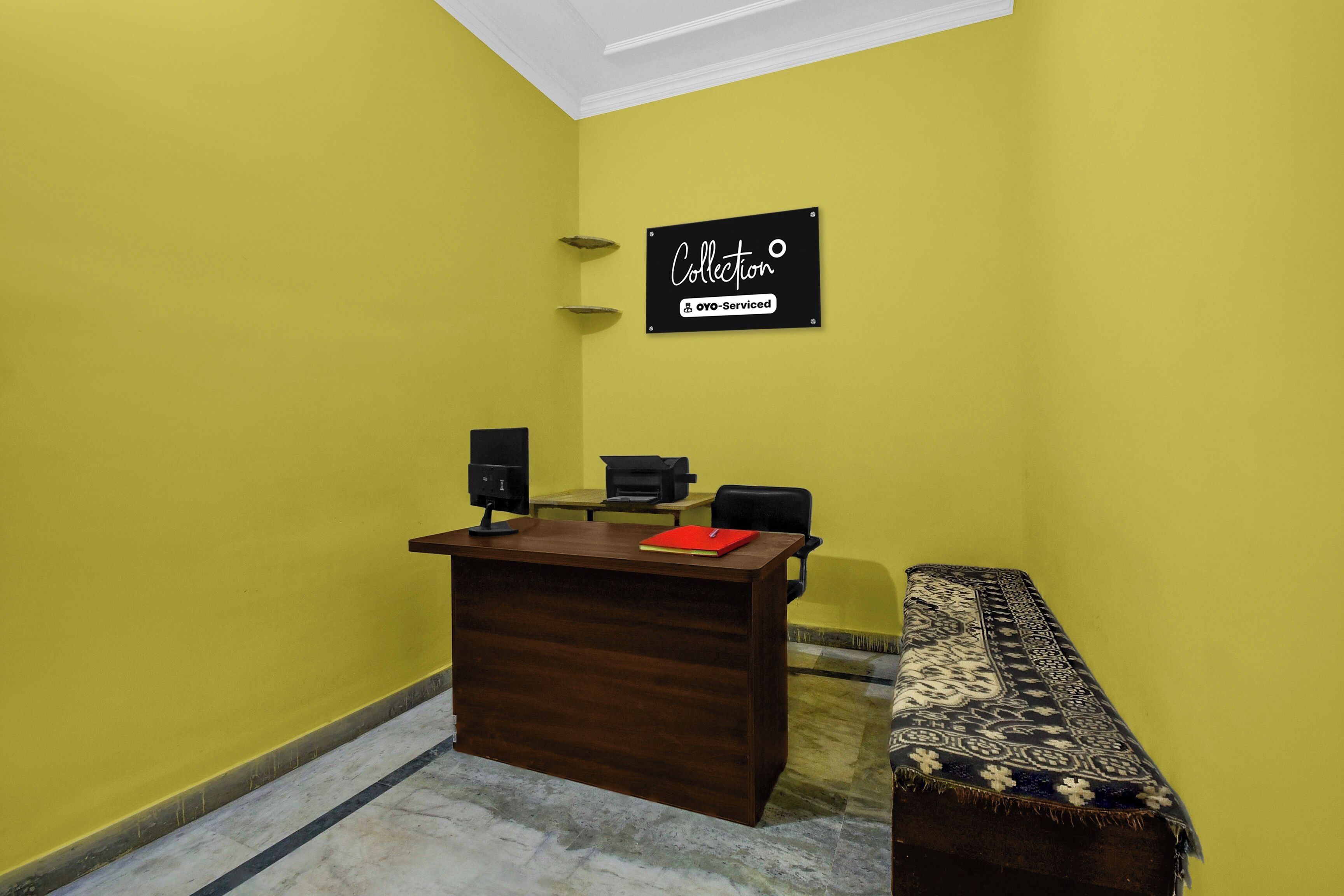 A reception desk with a computer, a printer, and a sign above it. There is a bench with a patterned cushion beside the desk.