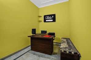 A reception desk with a computer, a printer, and a sign above it. There is a bench with a patterned cushion beside the desk. - Collection O JECC Jaipur (Jaipur)