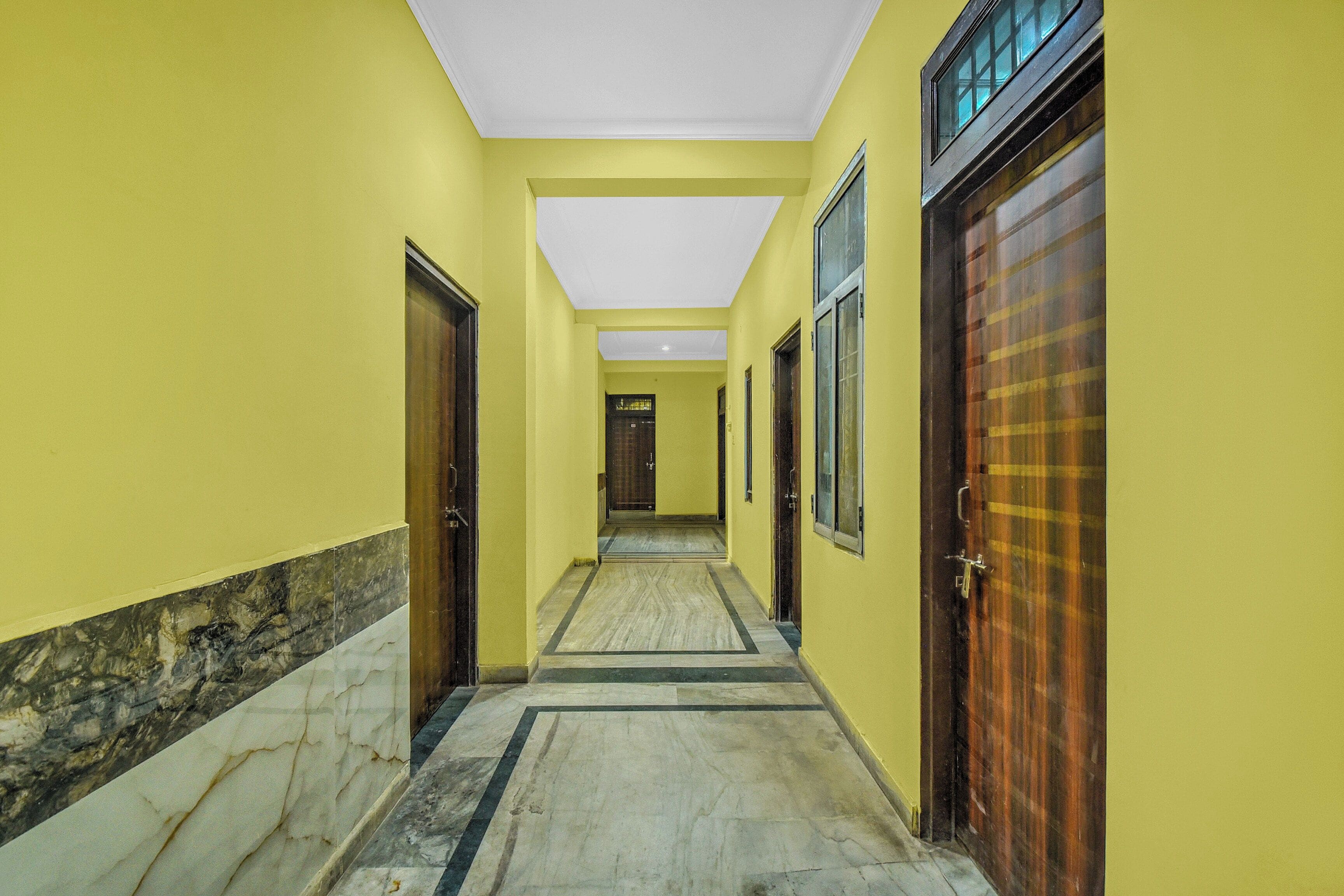 A corridor with yellow walls, marble flooring, and doors leading to rooms.