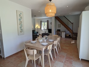 A dining area with a table set for four, a staircase, and a living room in the background. - Holiday Home 'La Valkyrie' with Mountain View, Wi-Fi and Air Conditioning (Caudiès-de-Fenouillèdes)