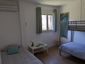 Et sovesal med køjesenge, et lille bord med bøger, et vindue med gardiner og et billede på væggen.