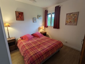 Une chambre à coucher avec un lit, deux lampes de chevet, une fenêtre avec des rideaux et des œuvres d’art murales.