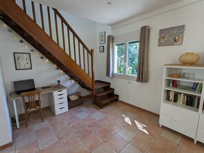 Une pièce avec un escalier en bois, un bureau avec un ordinateur portable, une bibliothèque et une fenêtre avec des rideaux.