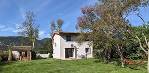 Une maison à deux étages, avec un toit en tuiles, une terrasse dotée de mobilier d’extérieur et un hamac.