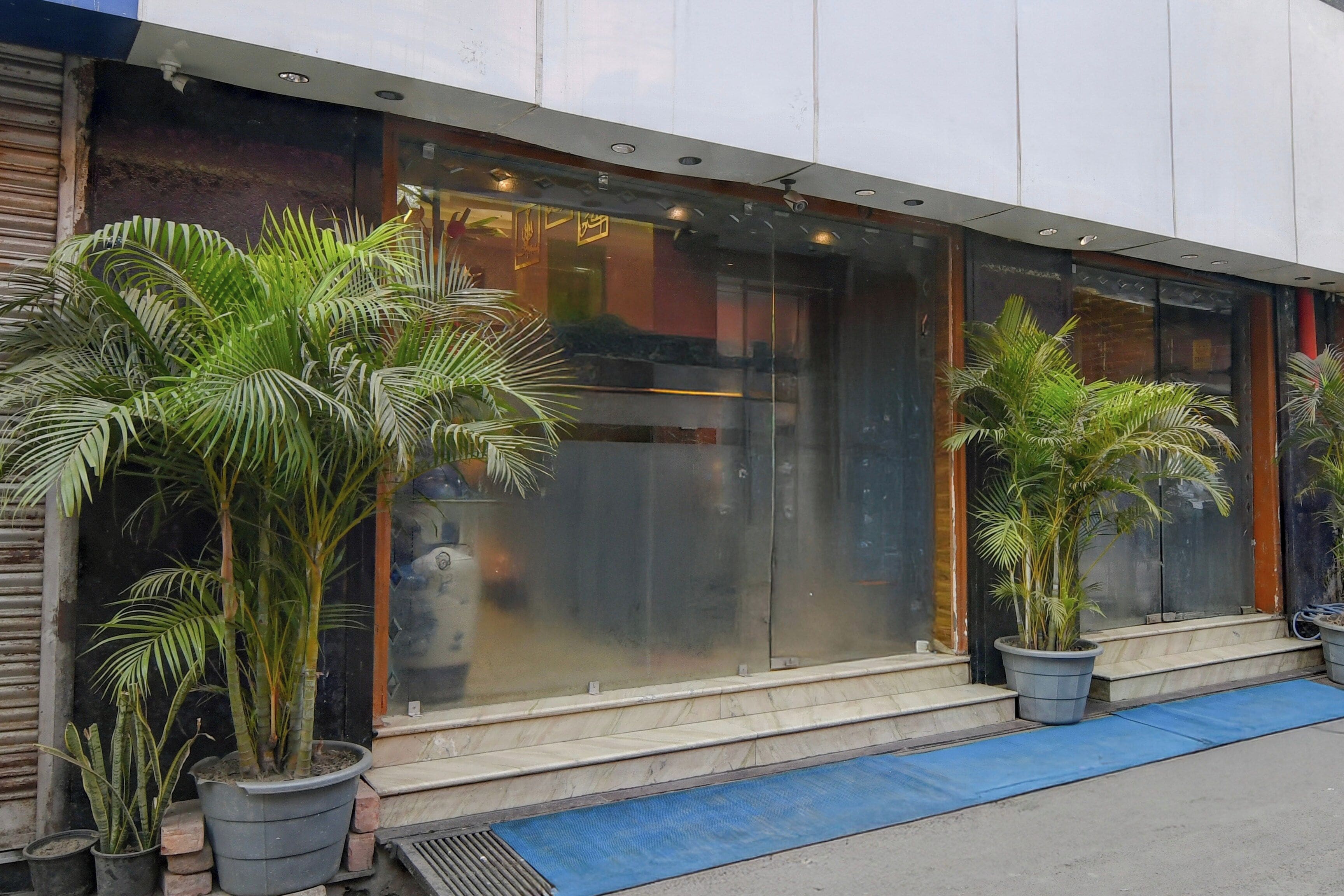 A building with large glass windows, potted plants, and a blue mat at the entrance.